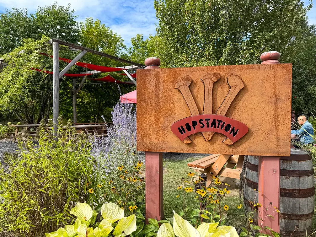 A sign for Hop Station brewery sits by a patio surrounded by plants and flowers