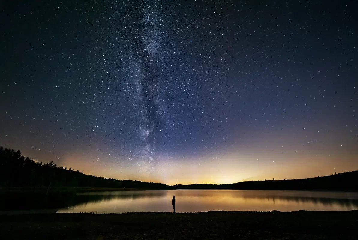 Man stands next to a lake beneath the Milky Way